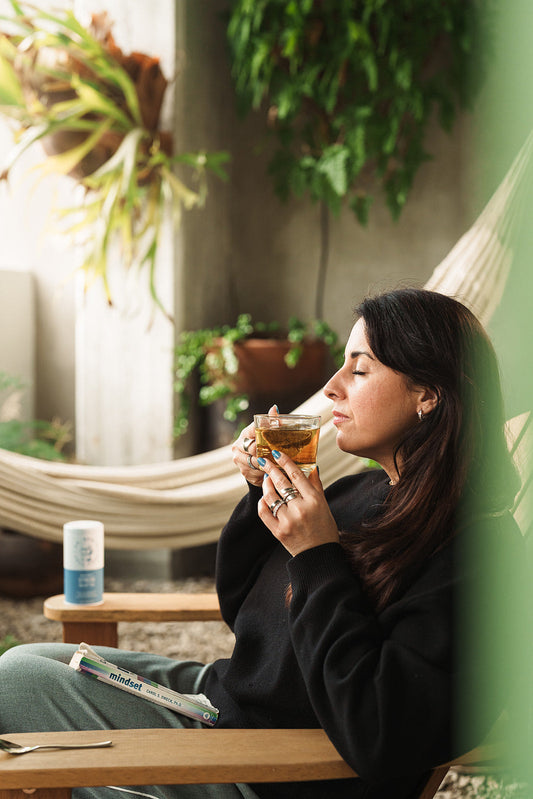 Woman relaxing with herbal tea surrounded by lush green plants, representing natural balance and calm