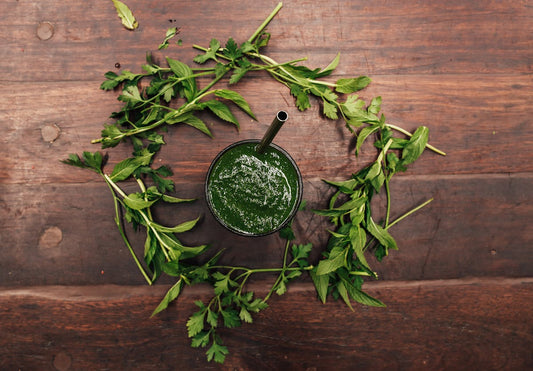 Fresh green smoothie surrounded by herbs on a wooden table - liver detox and natural wellness