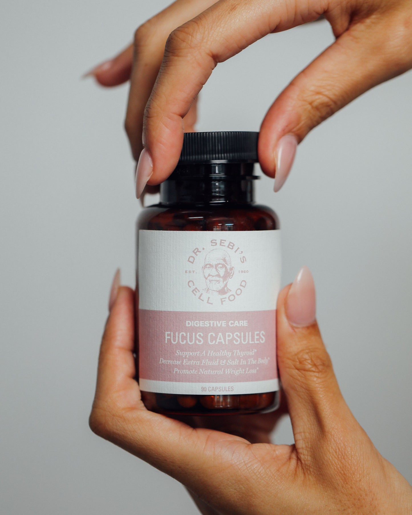 Hands holding Dr. Sebi's Digestive Care Fucus Capsules bottle against a neutral background.