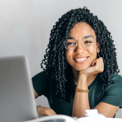 Smiling woman with glasses working at laptop, representing wellness and natural health consultation.