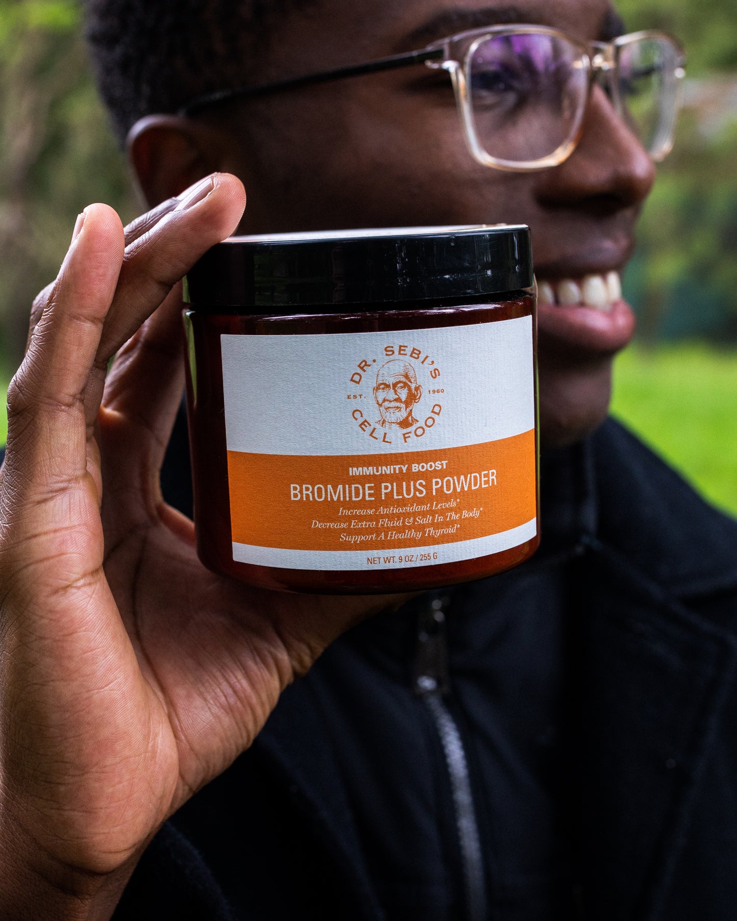 Person holding Dr. Sebi's Bromide Plus Powder bottle outdoors in natural daylight setting.