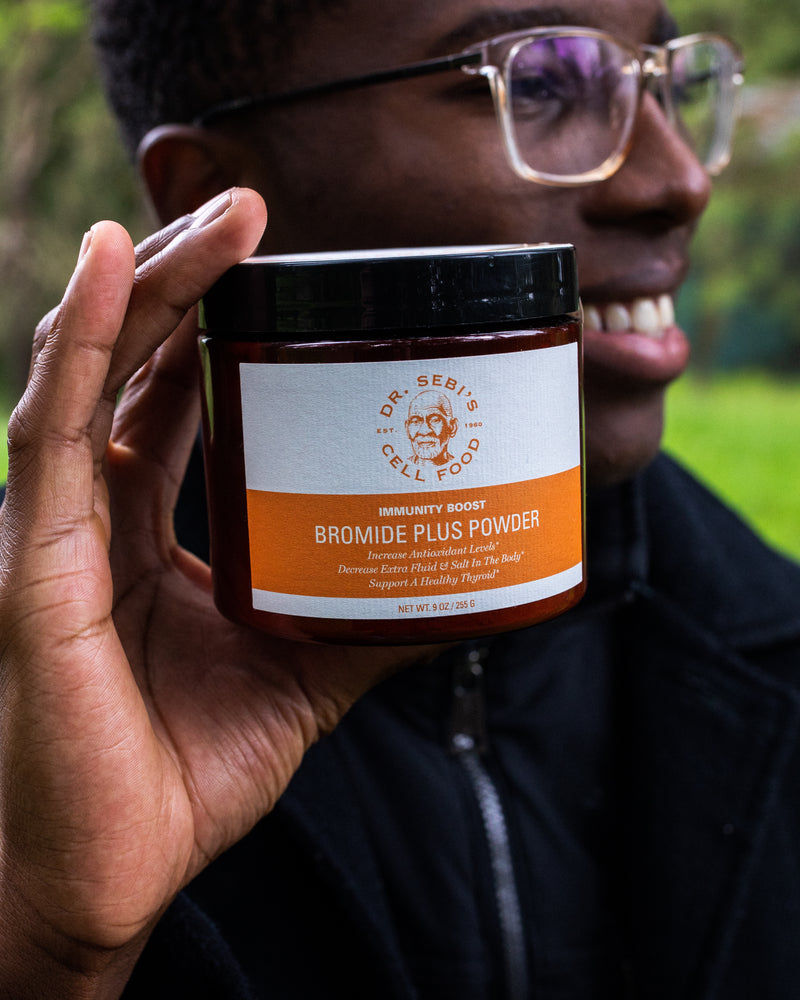 Person holding Dr. Sebi's Bromide Plus Powder bottle outdoors in natural daylight setting.