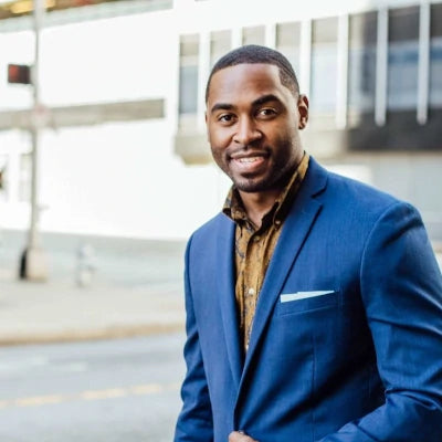 Professional man in blue blazer smiling at camera in modern office setting.