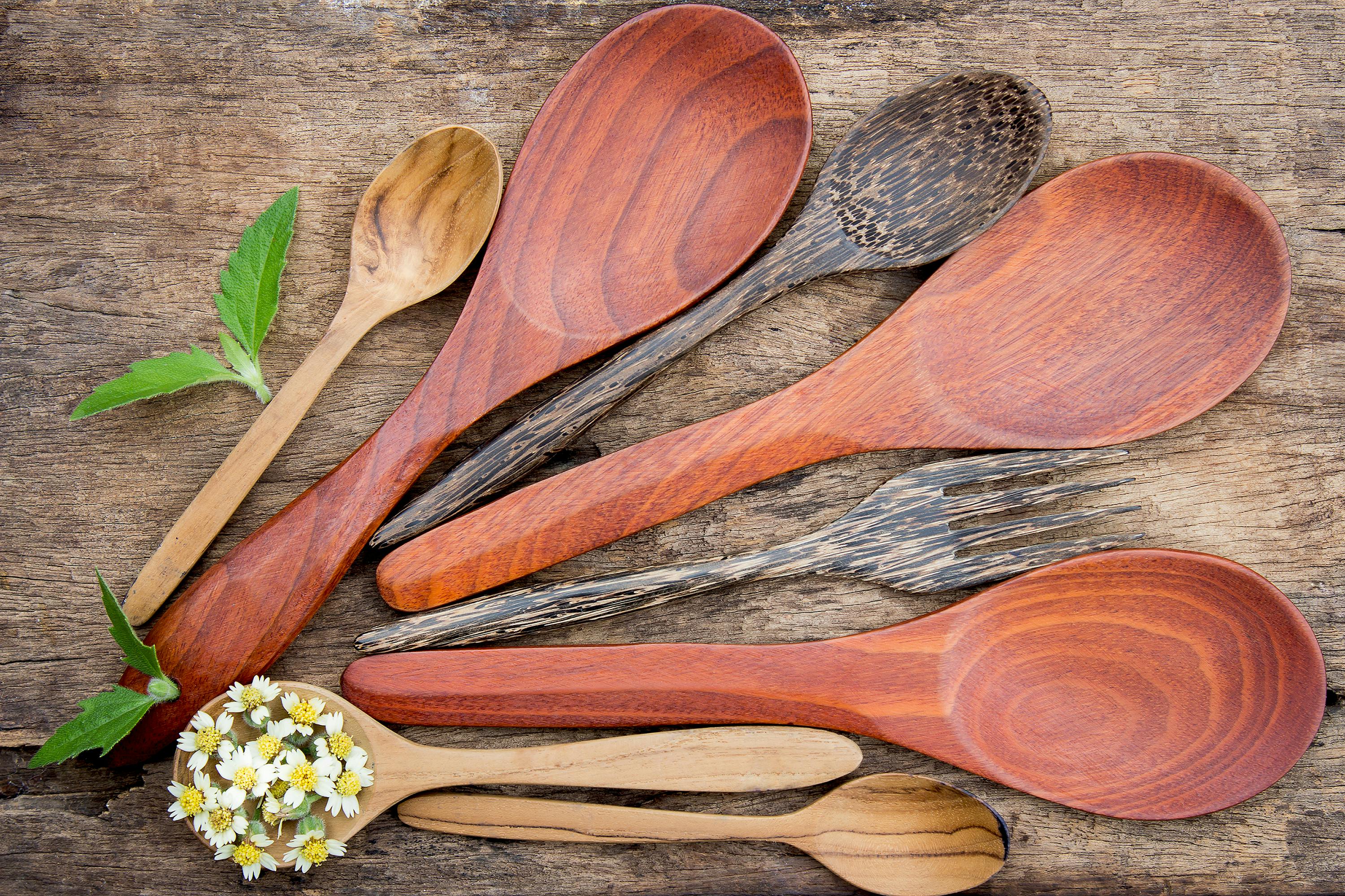 Collection of wooden spoons and utensils with fresh herbs and flowers on rustic wood surface.